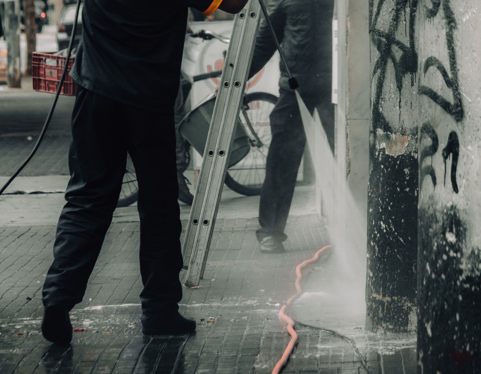 Workers cleaning graffiti off city building facade with a pressure hose.
